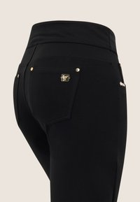 Mustat joustavat housut, joissa on sileä kangas, korkea vyötärö, erottuva kultainen varuste ja koristeelliset yksityiskohdat takataskuissa.