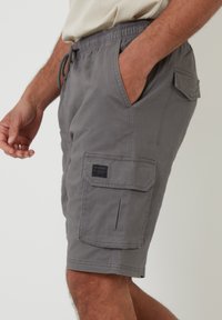 Pantalones cortos cargo grises hechos de una tela con una textura sutil, que cuentan con bolsillos laterales, un bolsillo trasero y una cintura ajustable con cordón.