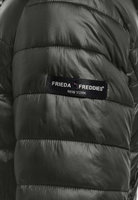 Zwarte gewatteerde jas met een gequiltetextuur. Beschikt over een zichtbare merketiket "Frieda Freddies New York" in een contrasterende donkere band.