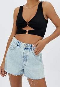 Top corto negro acanalado con corte frontal y detalle de hardware circular, combinado con pantalones cortos de mezclilla de tiro alto desgastados en azul claro.