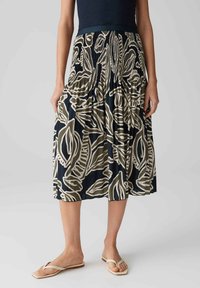 Gonna di lunghezza media di colore blu scuro con un motivo a foglie beige e oliva. Presenta una vita arricciata e tasche laterali. Tessuto leggero.