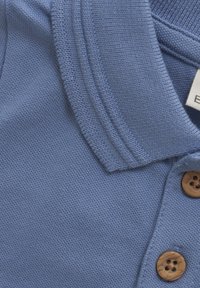 Blauwe polo gemaakt van gestructureerde katoen, met een kraag, drie bruine knopen en een label dat gedeeltelijk zichtbaar is bij de hals.