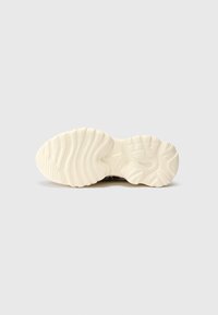 Sola de um ténis com uma espessa sola de borracha branca, apresentando ranhuras e padrões texturizados para tração, destacando uma forma arredondada.