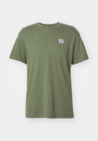 T-shirt in cotone verde oliva con maniche corte e scollatura a girocollo. Presenta un piccolo etichetta bianca e viola sulla parte sinistra del petto.