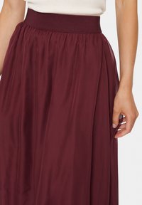 Faldă maxi burgundă cu un talie elastică înaltă, material ușor și design pliat pentru o siluetă fluidă.