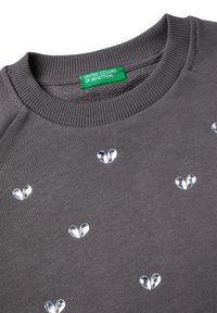 Felpa grigia con scollatura a coste, caratterizzata da decorazioni a forma di cuore trasparenti su tutta la superficie. L'etichetta riporta "UNITED COLORS OF BENETTON."