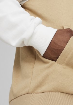 Sudadera beige con puños acanalados blancos. Incluye un bolsillo frontal con una costura limpia y un tejido suave y texturizado.