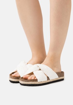 Hvide flettede slidesandaler med en vævet tekstur, kork mellemsål og sort gummisål. Åben tå-design fremhæver fødderne.