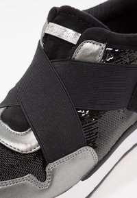 Czarne sneakersy z cekinowym wzorem, metalicznie srebrnymi akcentami, elastycznym paskiem na górze i białą podeszwą. Posiadają metkę z markowym logo.