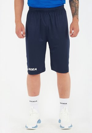 Uomo con pantaloncini sportivi LEGEA blu navy, calzini bianchi LEGEA e scarpe sportive bianche, in piedi davanti a uno sfondo uniforme.