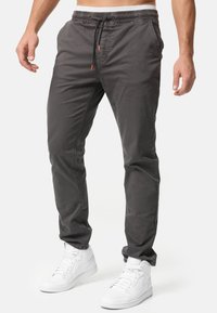 Pantalones gris de corte slim, fabricados en algodón ligero, con cintura elástica con cordón y bolsillos laterales, combinados con zapatillas blancas.