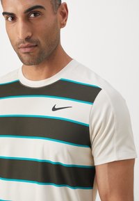 Hombre vestido con una camiseta blanca de manga corta con rayas horizontales negras y azules, y un logo negro de Nike en el pecho.