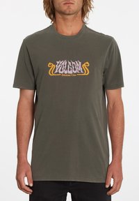 T-shirt en coton vert olive avec un logo graphique violet et jaune "VOLCOM Stone Co." sur la poitrine. Col rond et manches courtes.