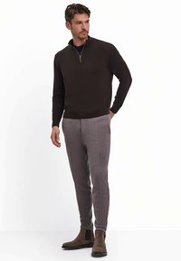 Pull marron à col zippé associé à un pantalon droit gris clair. Bottines marron mises en avant. Texture lisse et design structuré visibles.