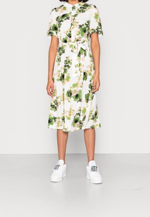 Blomstret kjole med korte ærmer, hvid baggrund, grønne og pink mønstre, taljesmæk, og design med knapper, kombineret med hvide sneakers.