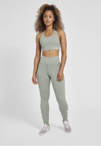 Ljusgrön sportbh och högmidjade leggings i slät tyg; har diskret sömnad och en logo på bh:n. Följt av grå sneakers.