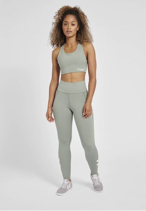 Hellgrüner Sport-BH und hochtaillierte Leggings aus glattem Stoff; mit subtilen Nähten und einem Logo auf dem BH. Begleitet von grauen Sneakers.