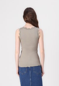 Olijfgroen geribbelde tanktop met gevlochten kantafwerkingen bij de schouders, aansluitende pasvorm en gebogen zoom. Gemaakt in combinatie met een spijkerrok.