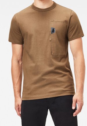 Brun kortærmet t-shirt lavet af bomuld. Har en lomme på venstre bryst med en kontrastknap og syede detaljer.