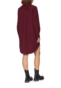 Bordeauxfarbenes Hemdkleid mit langen Ärmeln und einem Yoke-Detail im Rücken. Weicher Stoff und abgerundeter Saum. Kombiniert mit schwarzen Knöchelstiefeln.
