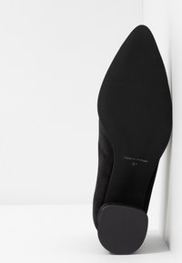 Semelle de chaussure noire à bout pointu avec un petit talon carré, indiquant "Made in Portugal" et la taille 37 imprimée en dessous.