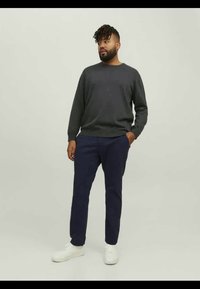 Σκούρο γκρι πλεκτό πουλόβερ, ναυτικού χρώματος παντελόνια και λευκά αθλητικά παπούτσια· άνετη εφαρμογή με στρογγυλή λαιμόκοψη, μανίκια με μανσέτες και πλαϊνές τσέπες.