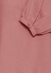 Lyserød tekstureret bluse med en manchet med knap. Stoffet har en subtil krølleeffekt og en afslappet pasform med en glat finish.