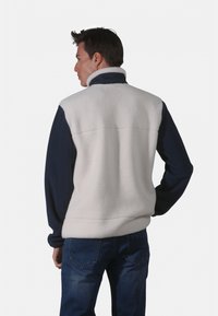 Veste en polaire avec un corps crème et des manches bleu marine. Présente un col montant et est fabriquée en tissu doux et texturé. Coupe décontractée, vue de dos.