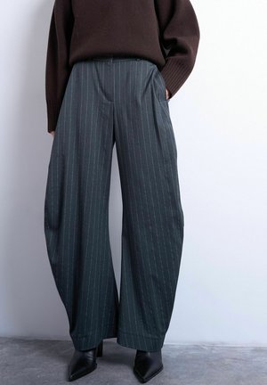 Vidde, mørkegrå bukser med fin stribe, kombineret med sorte spidse støvler og en mørkebrun langærmet sweater.