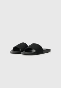 Black slide sandals made of soft fabric and rubber, featuring an open-toe design, wide straps, and embossed branding on the side.