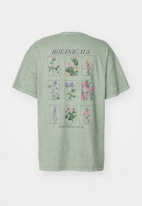 Zelené bavlněné tričko s botanickým potiskem obsahující devět květinových ilustrací, text "BOTANICALS" a "KEEPTHINGSWILD" v černé barvě.