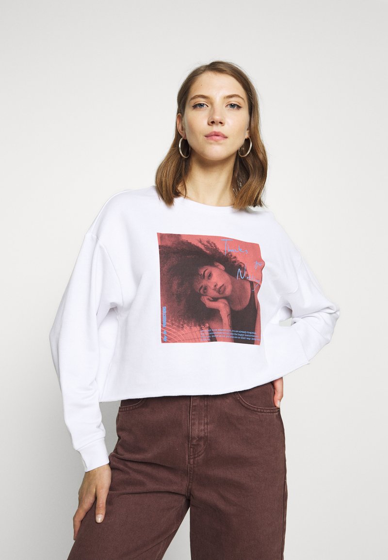 Sweatshirt curto branco com uma estampagem gráfica apresentando uma mulher em tons de vermelho. Mangas longas, decote arredondado e um corte descontraído.