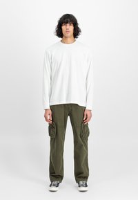 Witte lange mouwen t-shirt gecombineerd met olijfgroene cargo broek met grote zijzakken, afgemaakt met zwart-witte sneakers.