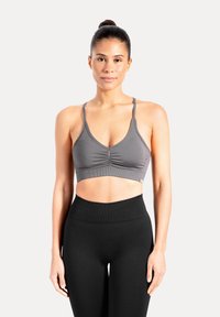 Grijze sportbeha met dunne bandjes en geplooide details aan de voorkant, gecombineerd met zwarte, hoge taille legging van rekbare stof.