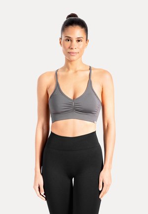 Harmaa urheiluliivit, joissa on ohuet olkaimet ja edessä poimuttettu yksityiskohta, yhdistetty korkeavyötäröisiin mustiin leggingsseihin, jotka on valmistettu joustavasta materiaalista.