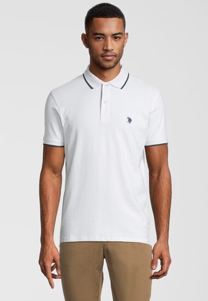 Camisa polo blanca de manga corta, con cuello y acentos de manga en color navy, que presenta un pequeño logotipo bordado en el lado izquierdo del pecho.