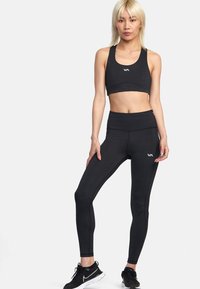 Set di reggiseno sportivo nero e leggings, realizzato in tessuto elastico. Caratterizzato da una texture liscia, design aderente e dettaglio con logo bianco sul lato sinistro.