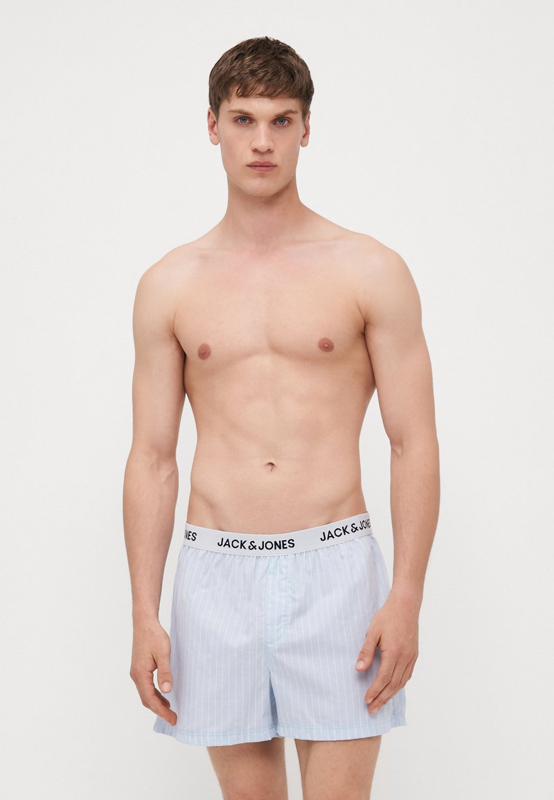 Boxers rayés bleu clair avec une ceinture élastique noire portant l'inscription "JACK & JONES." Le tissu semble lisse et léger.