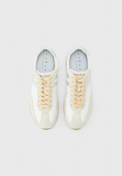 Ζευγάρι λευκά αθλητικά παπούτσια χαμηλού τύπου με μπεζ κορδόνια και ανοιχτό γκρι ρίγες στο πλάι, από πάνω, σε απλό φόντο.