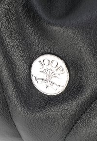 Borsa a tracolla in pelle nera con texture, caratterizzata da un logo circolare in argento con design floreale e il testo "JOOP! JEANS."