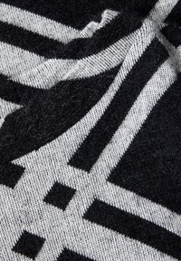 Svart- och grårandig tyg, med en mjuk struktur och en fluffig yta. Geometriskt mönster med växelvis tjocka och tunna linjer.