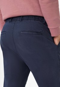 Pantaloni blu navy con finitura testurizzata, cintura elastica e due tasche posteriori con aperture orizzontali.