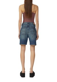 Dżinsowe szorty z postrzępionymi krawędziami, w niebieskim kolorze, z wysokim stanem. Tylne kieszenie ozdobione dekoracyjnym przeszyciem. Noszone z dopasowaną bluzką i butami na platformie.