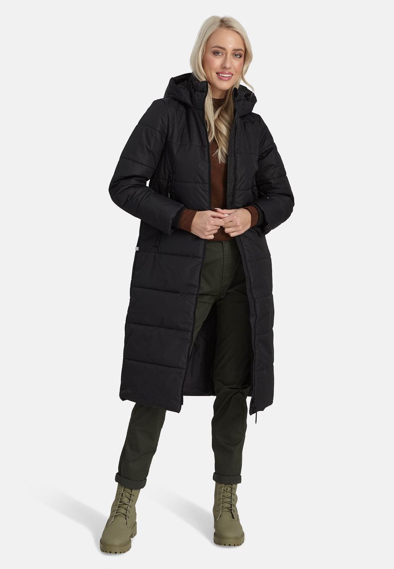 Melnā polsterētā garā jaka ar kapuci, ar rāvējslēdzēju, divām priekšējām kabatām un pamatni ar kviltnējumu. Valkāta virs brūna tops un zaļajām biksēm.