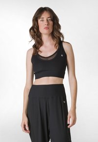 Svart atletisk crop top med nätöverdrag, elastisk band och logodetalj. Matchad med svarta ribbade vida byxor.