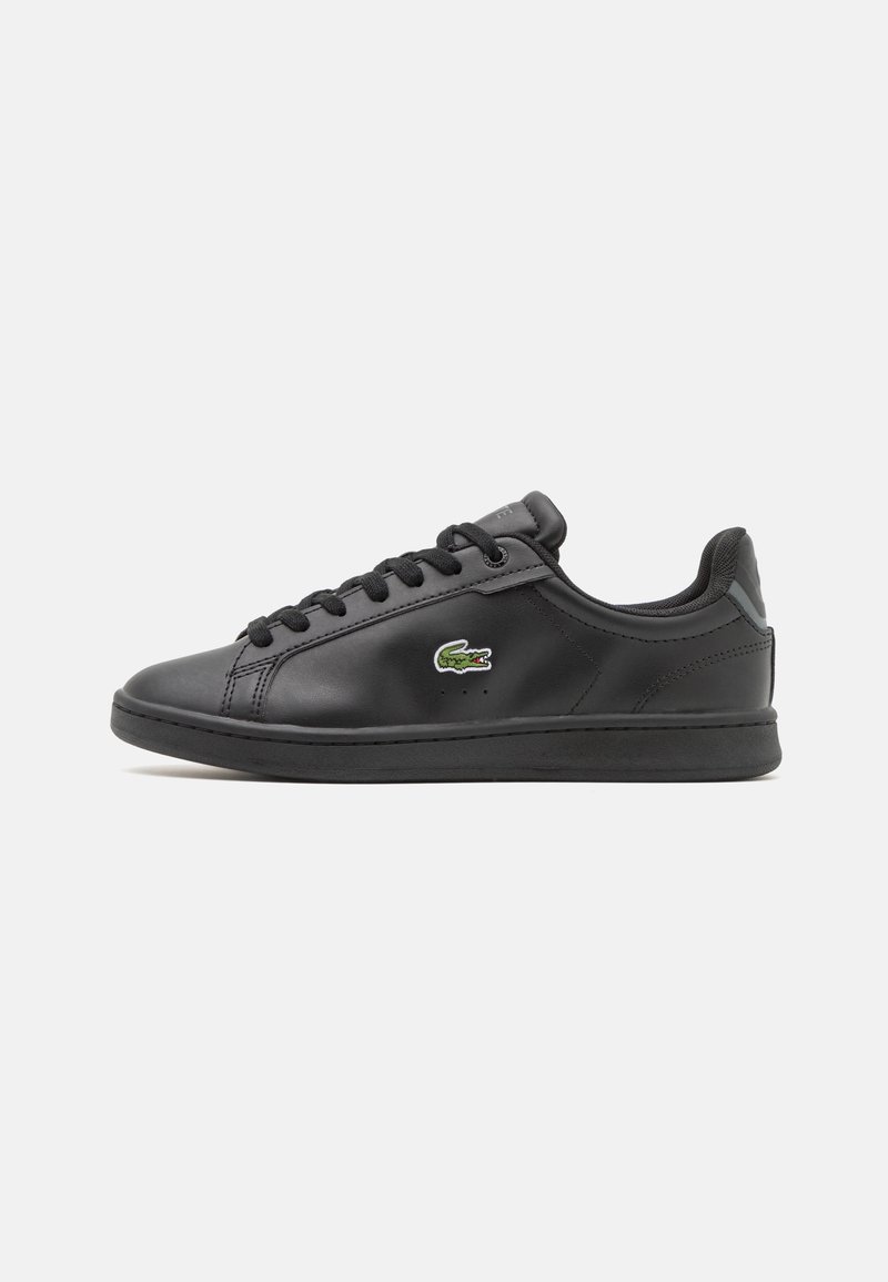 Baskets basses noires avec lacets et semelle noirs, avec un logo crocodile vert et blanc sur le côté.