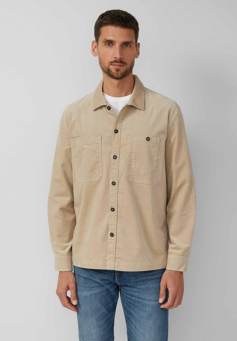 Bežová košeľa na gombíky z bavlnenej látky s golierom, dvoma náprsními vreckami a tmavými gombíkmi. Dlhé rukávy a rovný strih.
