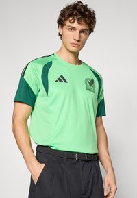 Green athletic T-shirt with darker green sleeves, featuring a textured fabric, the Mexico national team logo, and black Adidas stripes.