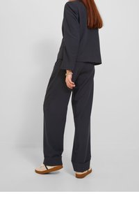 Černá saka a široké kalhoty se strukturovaným designem. Souprava má hladkou texturu, volný střih a je doplněna béžovou obuví.