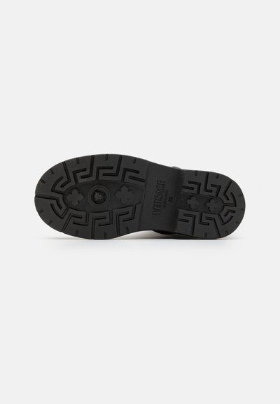 Semelle de chaussure en caoutchouc noir avec un motif de bande. Présente un logo en évidence et des designs géométriques, assurant adhérence et durabilité.
